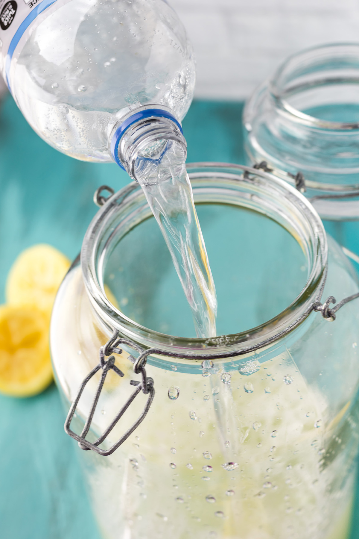 Pouring sparkling water into a glass jar to make homemade spiked lemonade.
