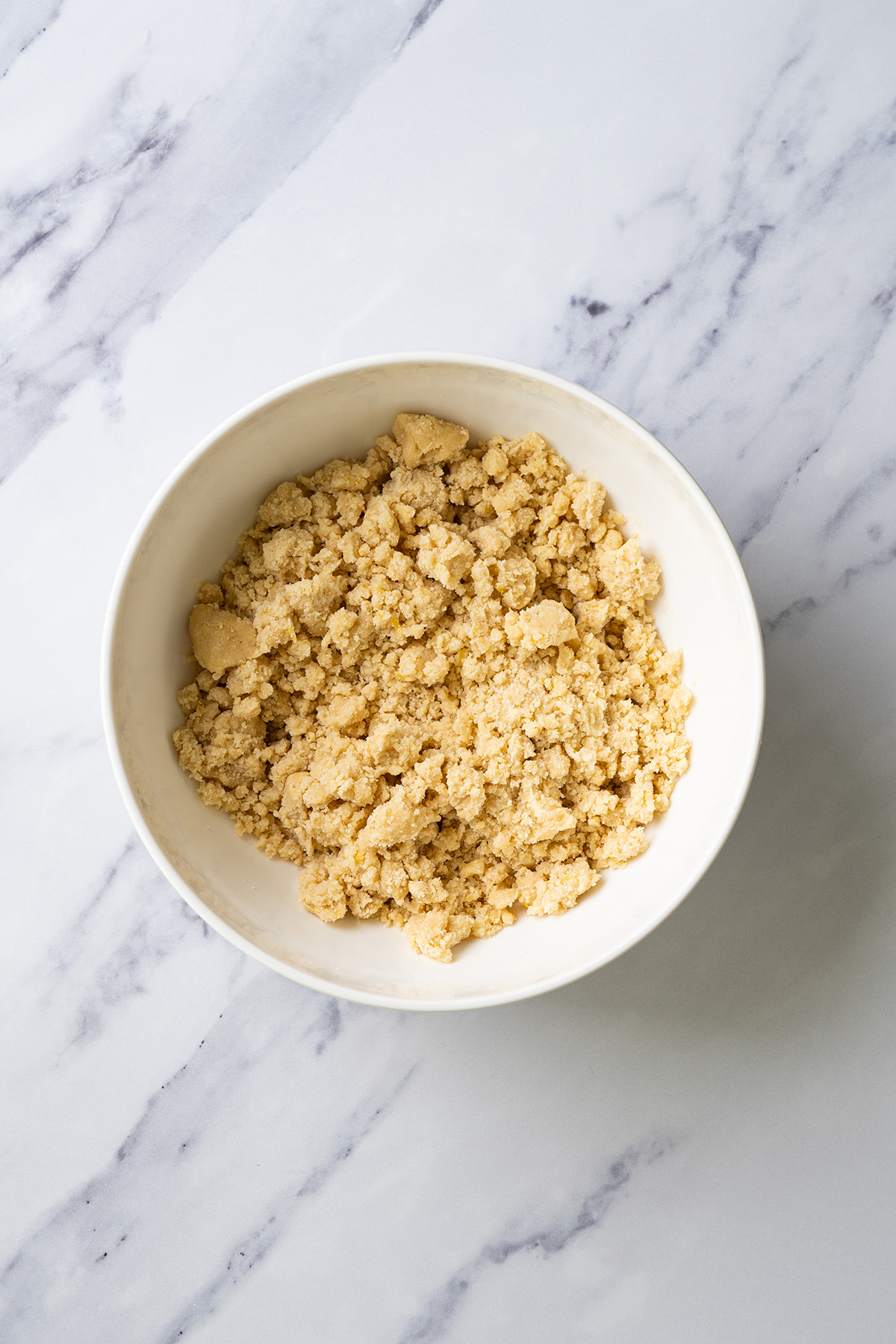 Crumbly cookie dough mixture in a white bowl, showing the texture before forming into balls.
