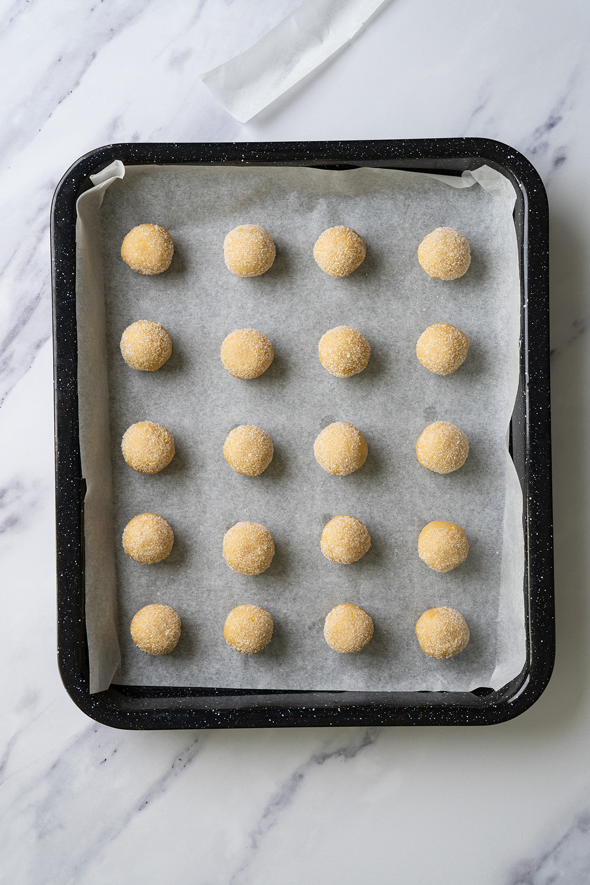 Unbaked sugar-coated cookie dough balls arranged evenly on a parchment-lined baking sheet.