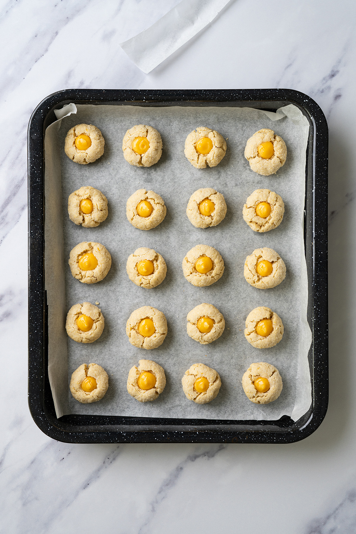 Lemon thumbprint cookies baked on a parchment-lined baking sheet, each filled with bright yellow lemon curd centers.