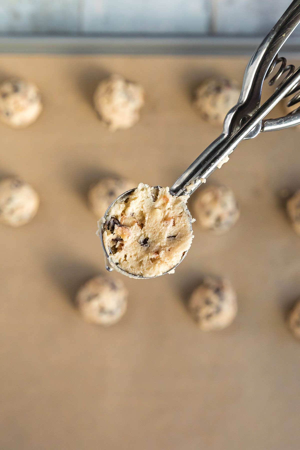 Scooping strawberry snowball cookie dough with a small cookie scoop onto a baking sheet.