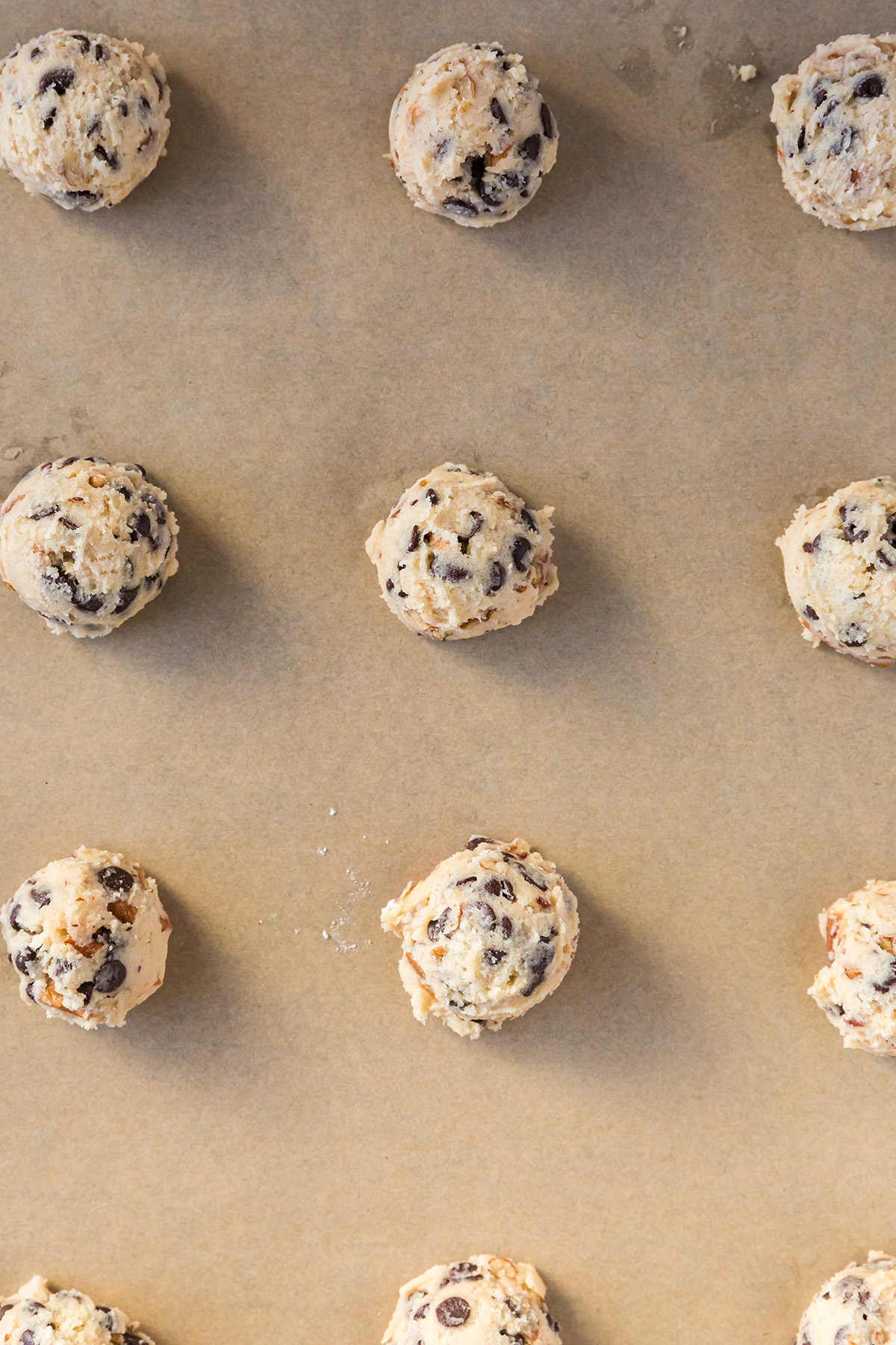 Unbaked strawberry snowball cookie dough balls arranged on a parchment-lined baking sheet.