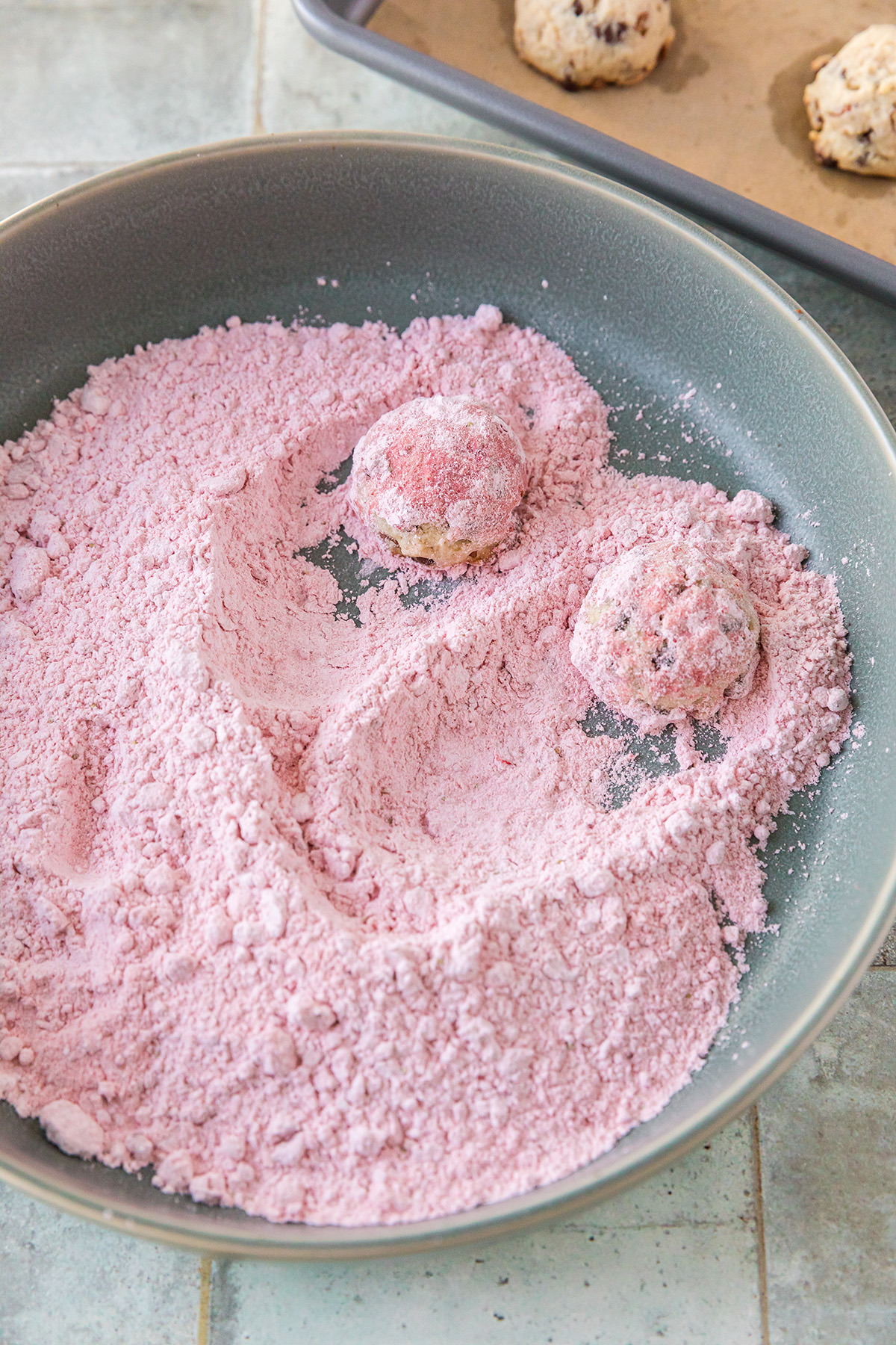 Warm strawberry snowball cookies being rolled in pink strawberry powdered sugar.