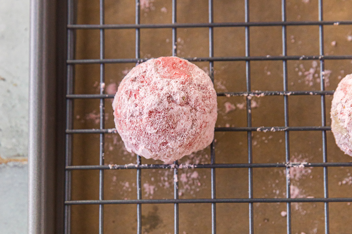 Strawberry snowball cookies coated in powdered sugar cooling on a wire rack.