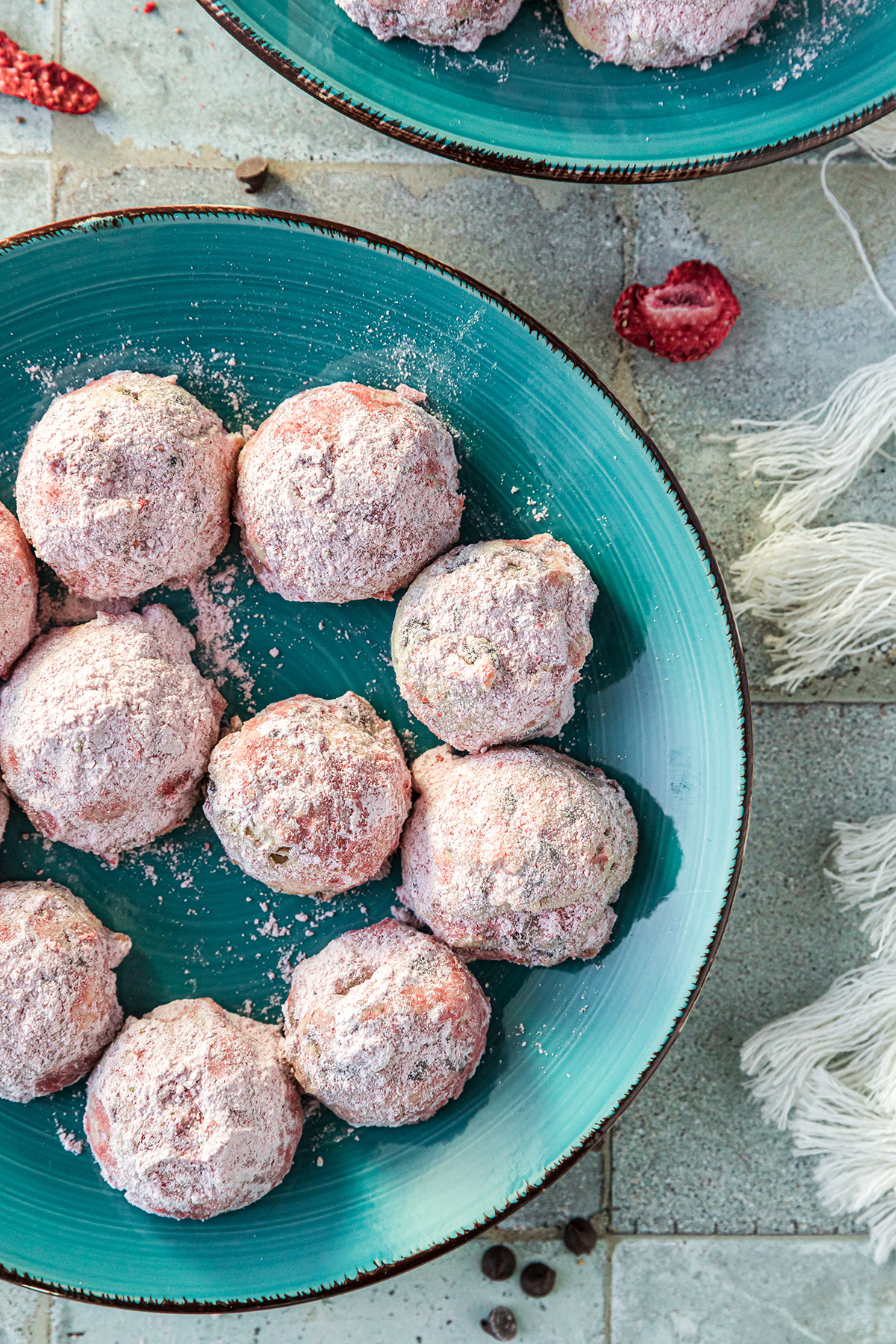 Strawberry snowball cookies coated in pink powdered sugar arranged on a teal plate.