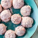 Strawberry snowball cookies coated in powdered sugar on a teal plate for serving.