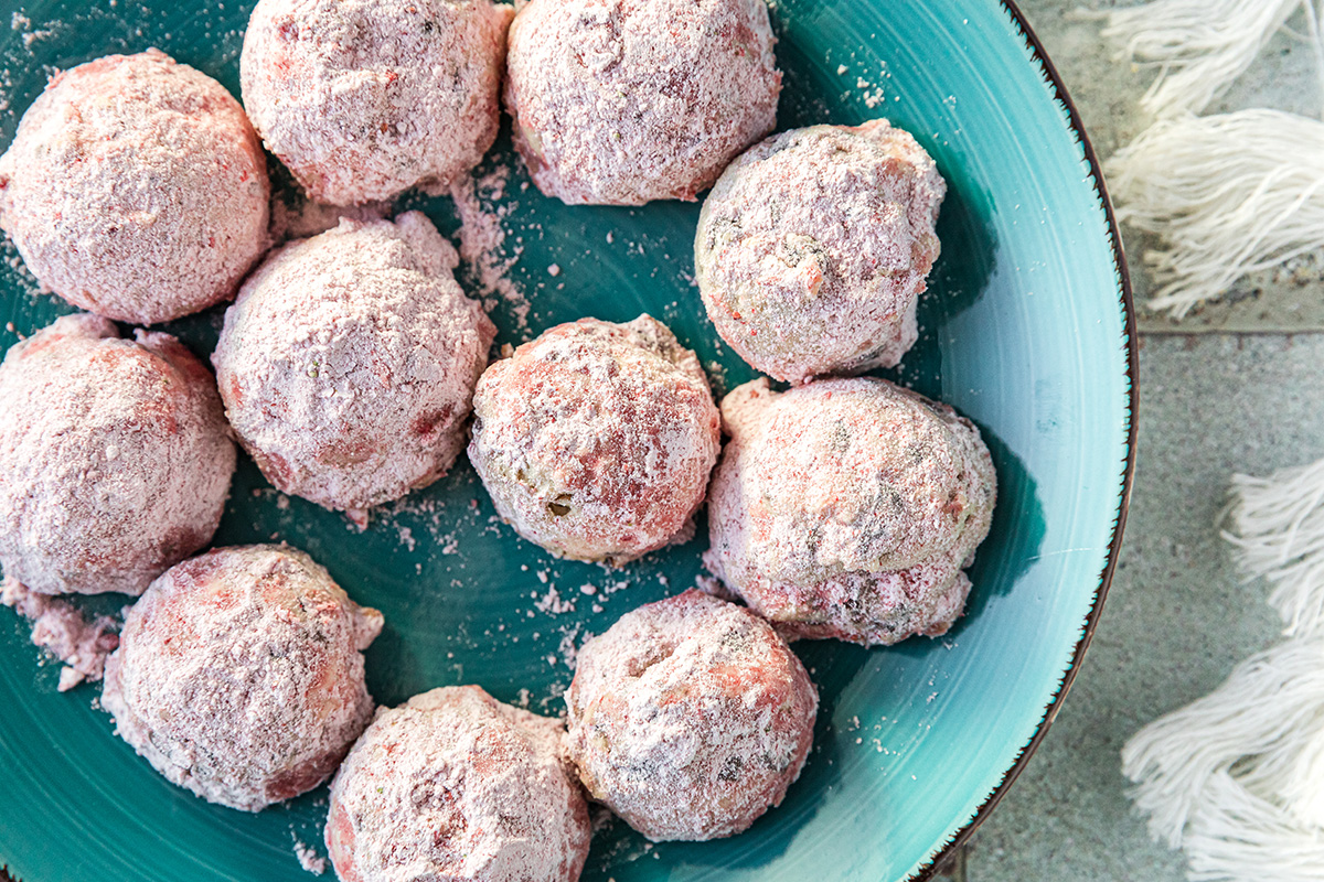 Strawberry snowball cookies coated in powdered sugar on a teal plate for serving.