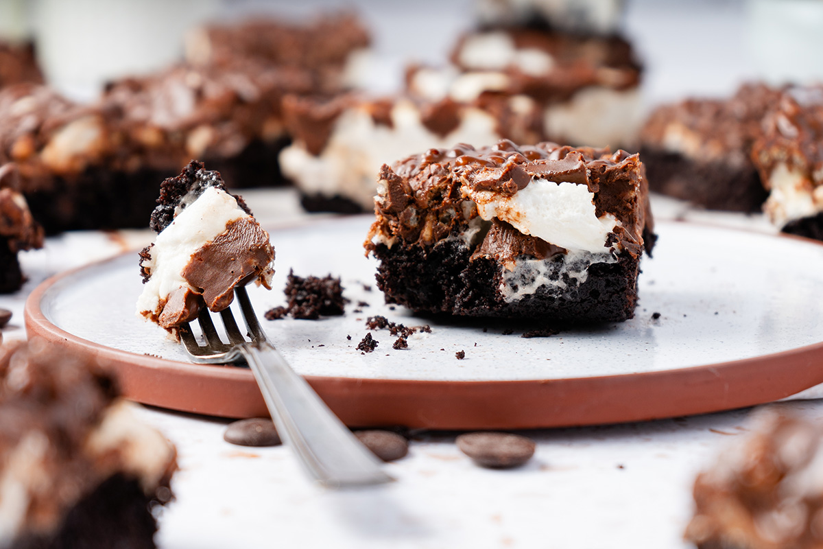 A fork lifting a bite of chocolate peanut butter crunch brownies with marshmallow and Rice Krispie topping.