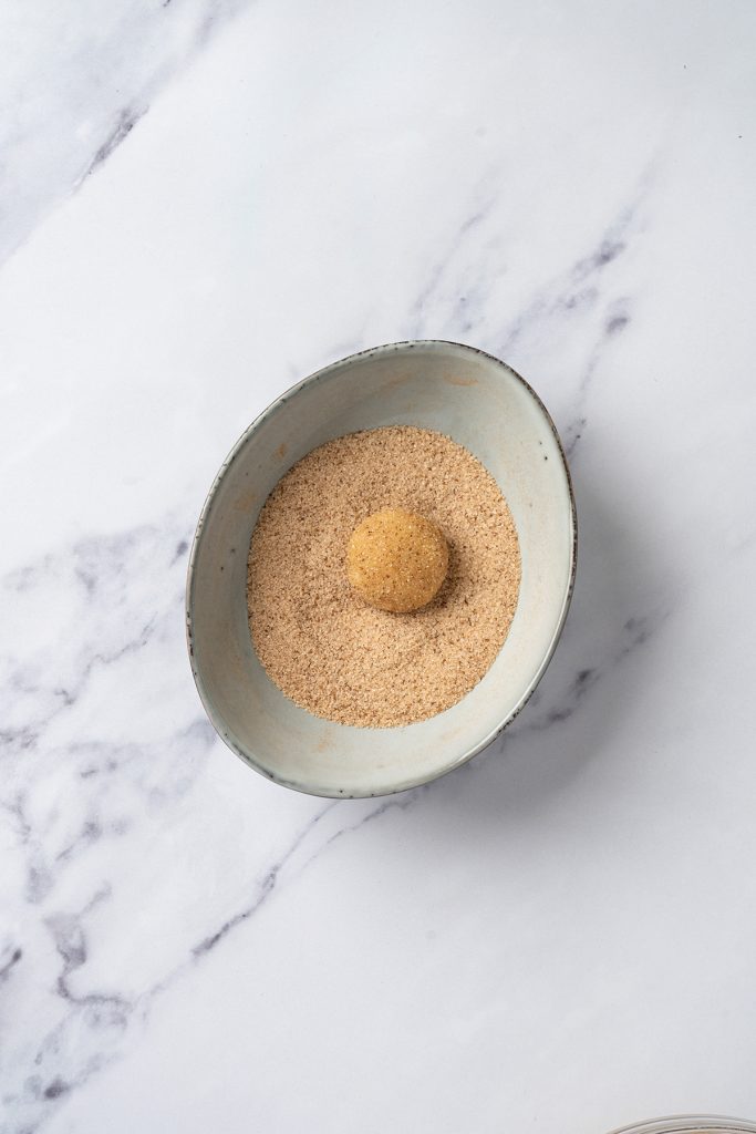 Ball of churro cookie dough rolled in cinnamon sugar before baking.