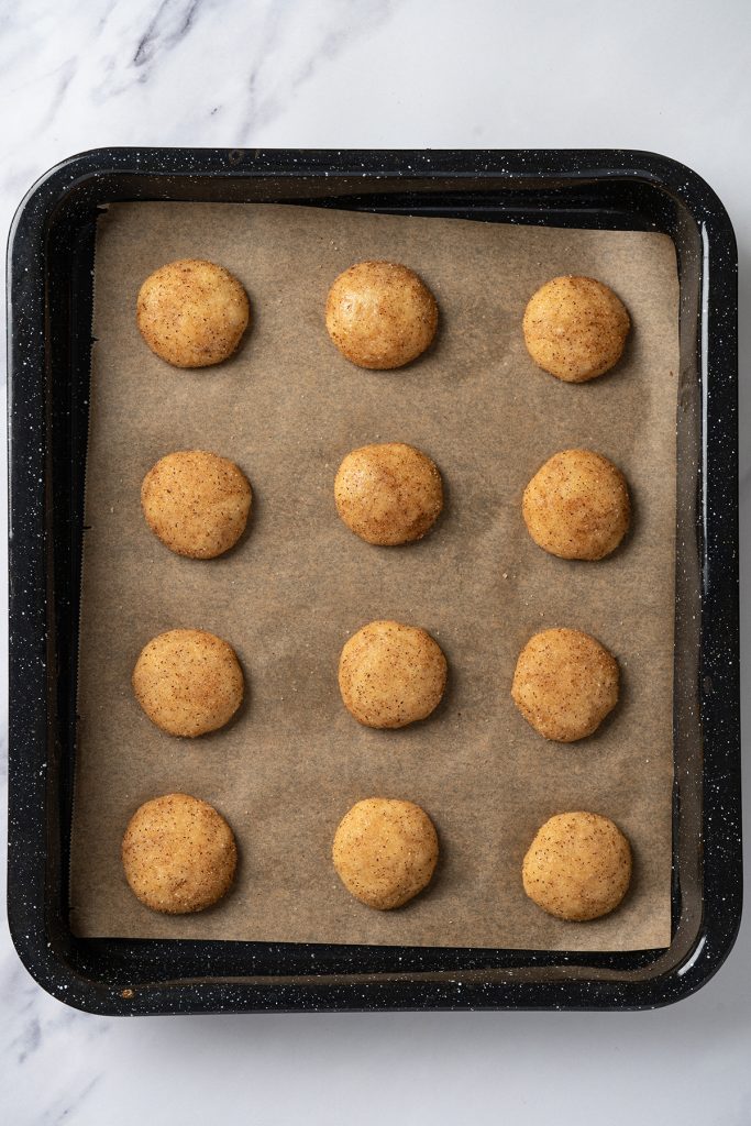 Cinnamon sugar coated cake mix cookie dough balls on a parchment lined baking sheet.