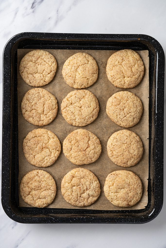 Freshly baked churro cookies cooling on a parchment lined baking sheet.