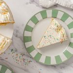 Slice of sugar cookie cake served on a green striped plate with vanilla buttercream and rainbow sprinkles.