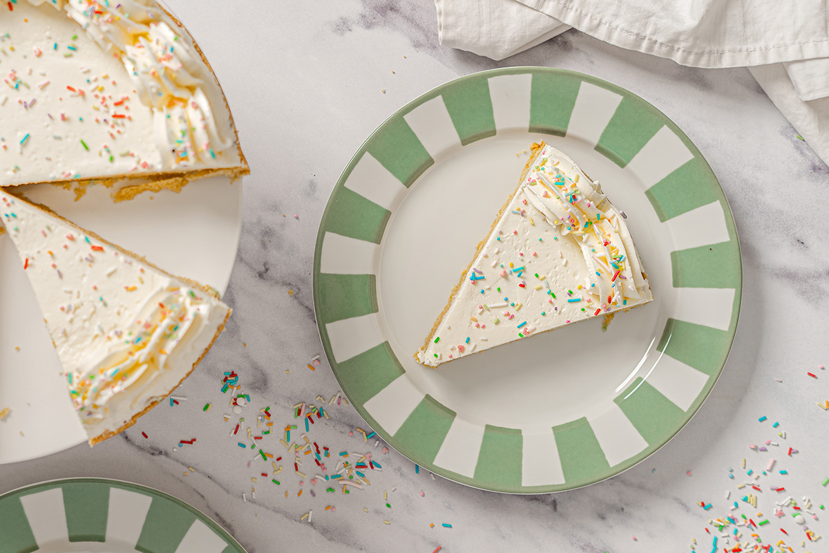 Slice of sugar cookie cake served on a green striped plate with vanilla buttercream and rainbow sprinkles.
