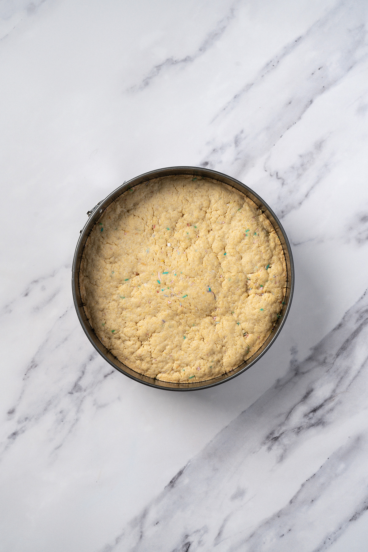 Baked sugar cookie cake in a springform pan, lightly golden on top and ready to cool before frosting.
