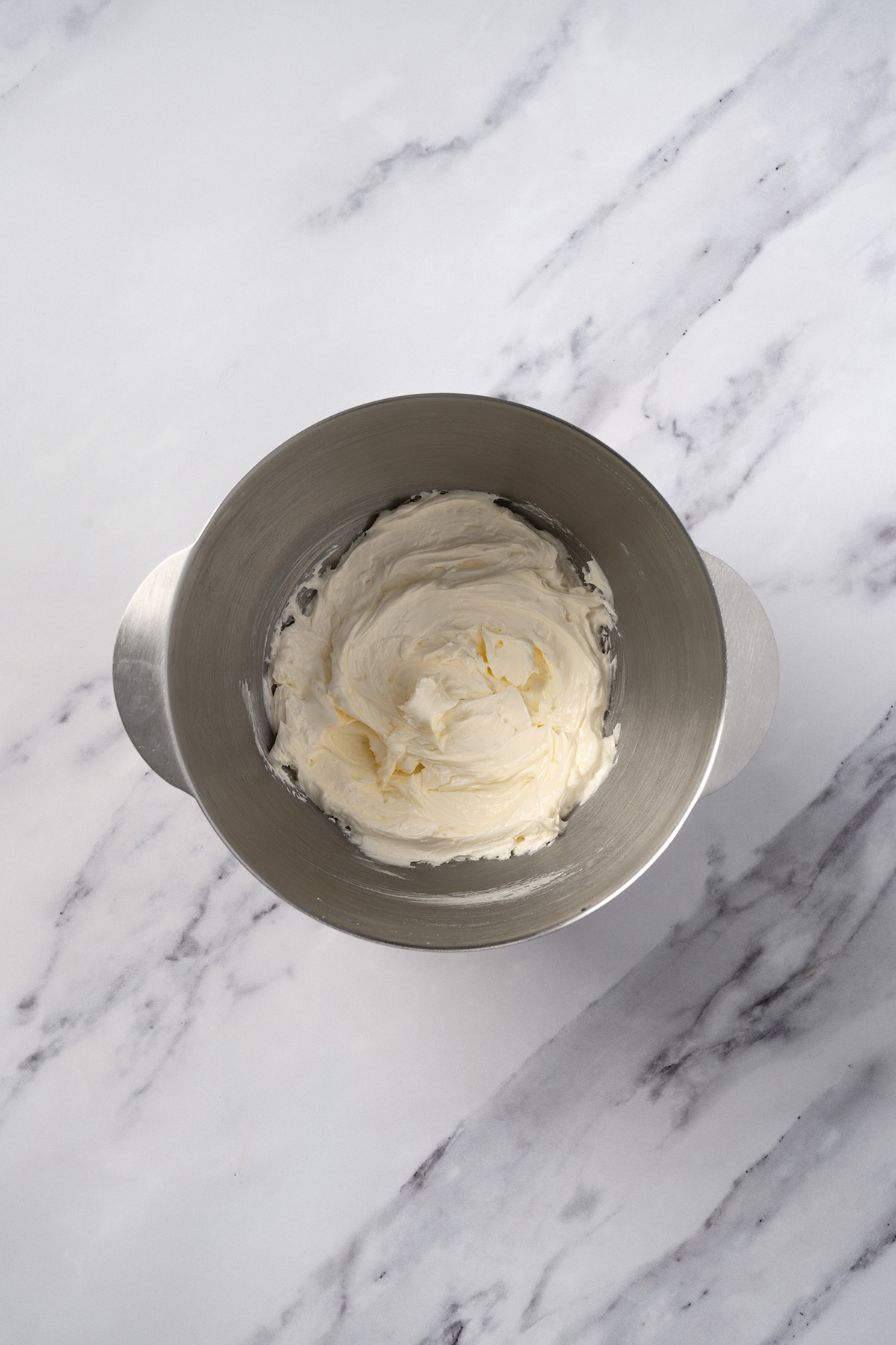 Whipped vanilla buttercream frosting in a stand mixer bowl, ready to spread over the cooled sugar cookie cake.