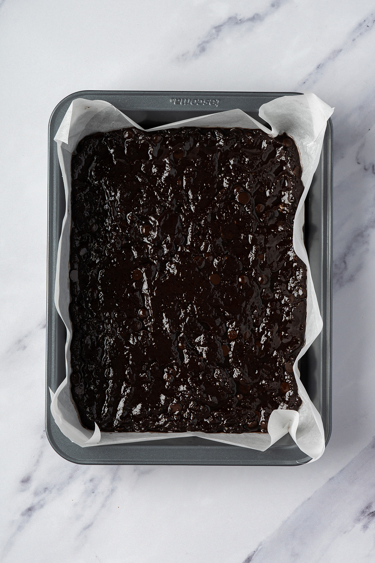 Chocolate brownie batter spread into a parchment-lined pan before adding the marshmallow and peanut butter krispie topping.
