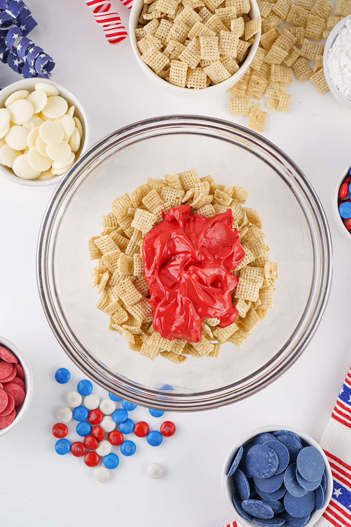 Chex cereal topped with melted red candy coating in a glass mixing bowl.