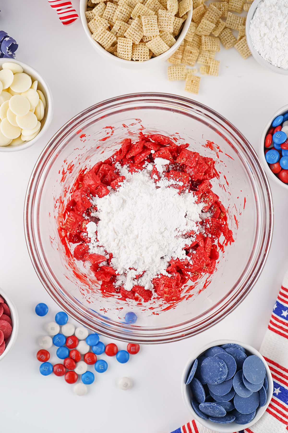 Red candy coated Chex cereal tossed with powdered sugar in a glass bowl for patriotic puppy chow.