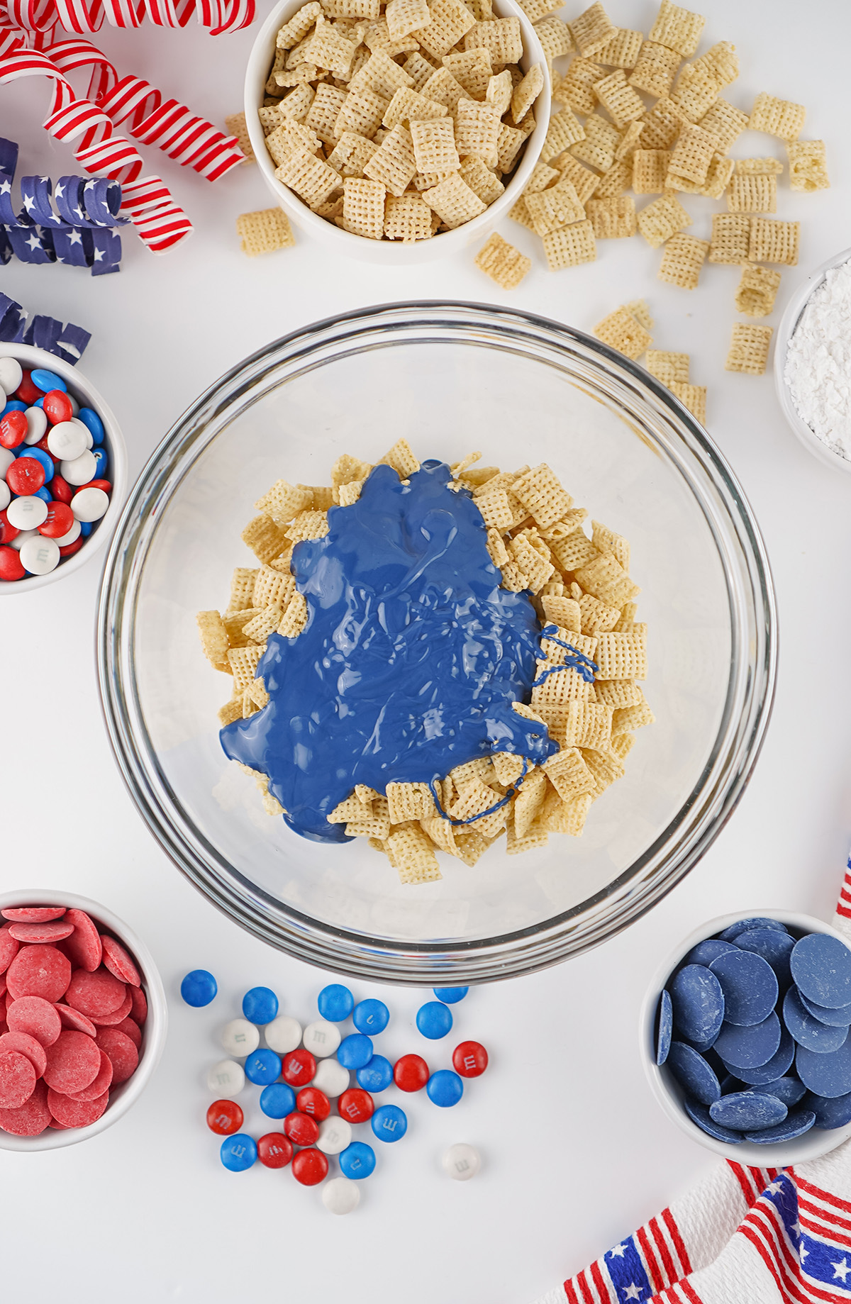 Blue candy melts poured over Chex cereal in a mixing bowl for red white and blue puppy chow.