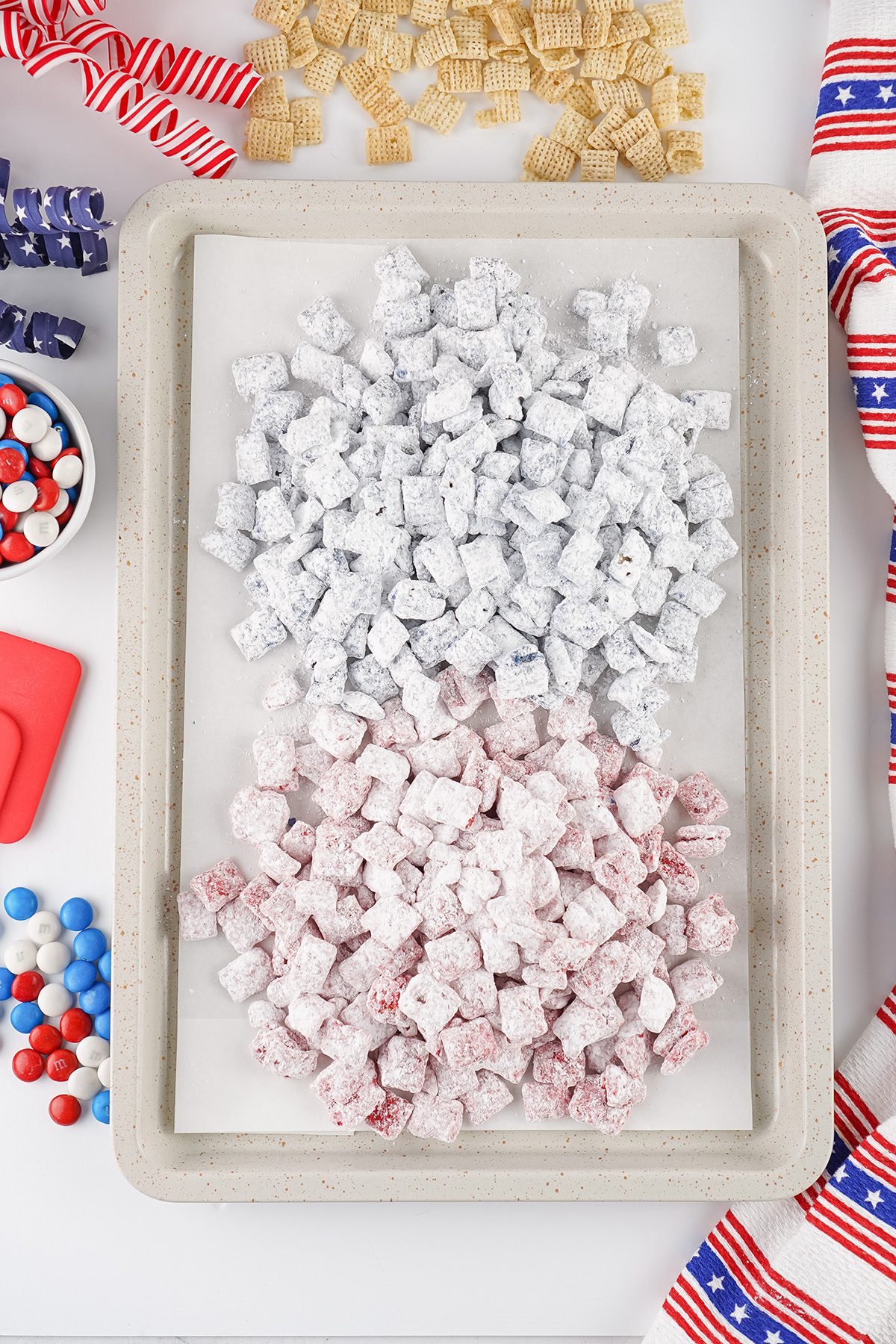 Red and blue puppy chow spread on a parchment lined baking sheet to dry.