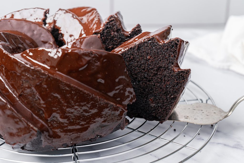 Slice of fudgy chocolate brownie cake being lifted from the Bundt cake with a cake server.