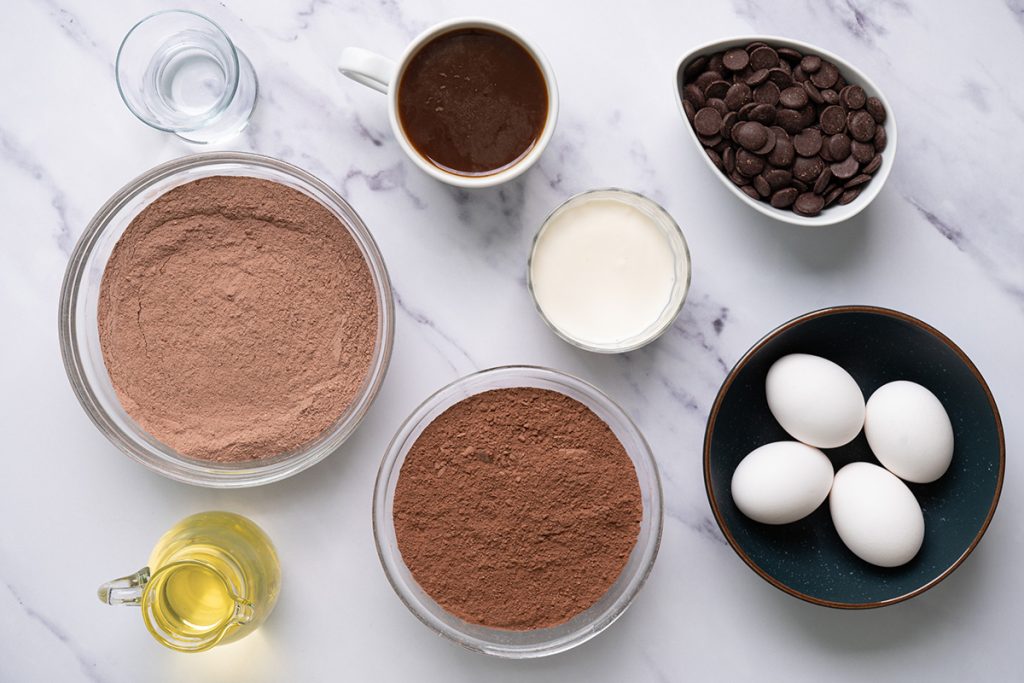 Ingredients for chocolate brownie cake including cake mix, brownie mix, eggs, coffee, oil, cream, and chocolate chips.
