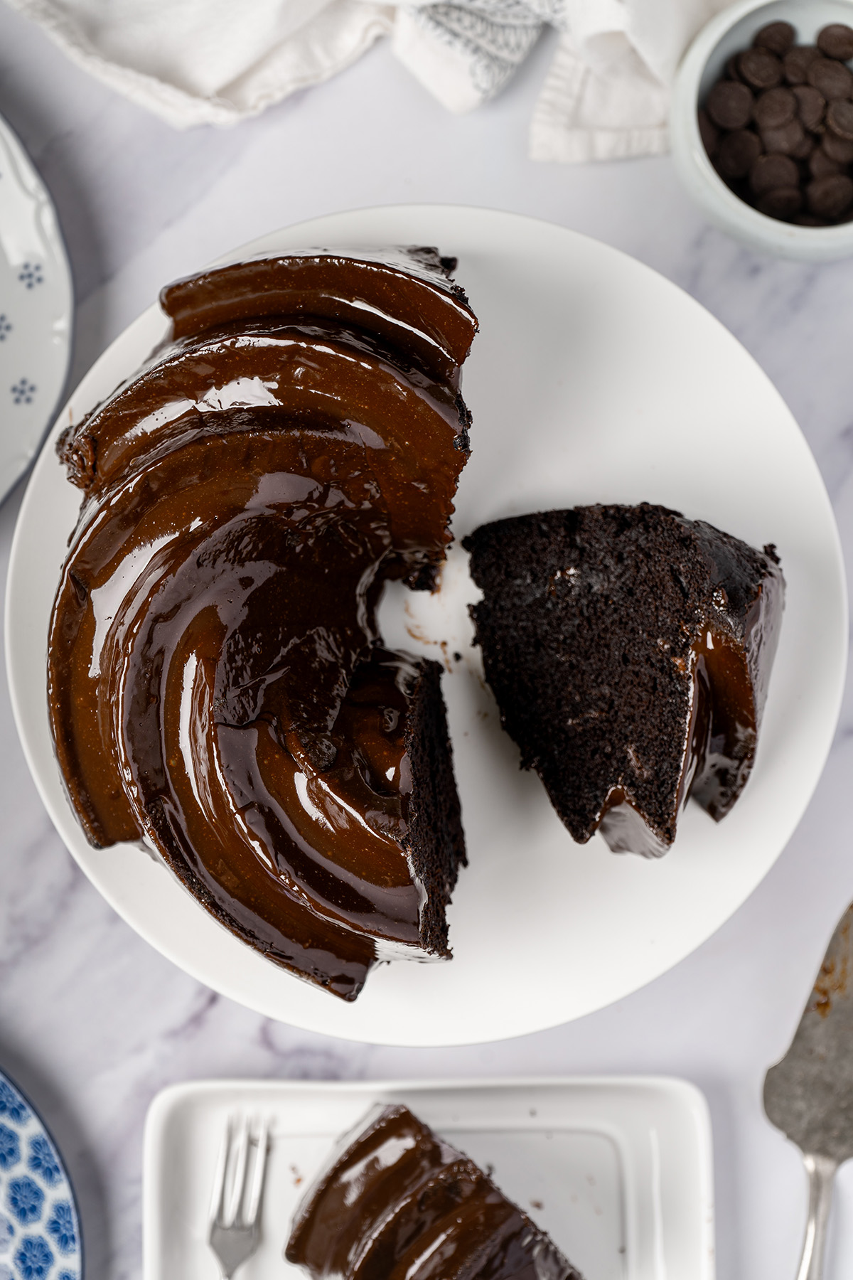 Fudgy chocolate brownie cake on a white plate with a slice cut out and glossy chocolate ganache on top.