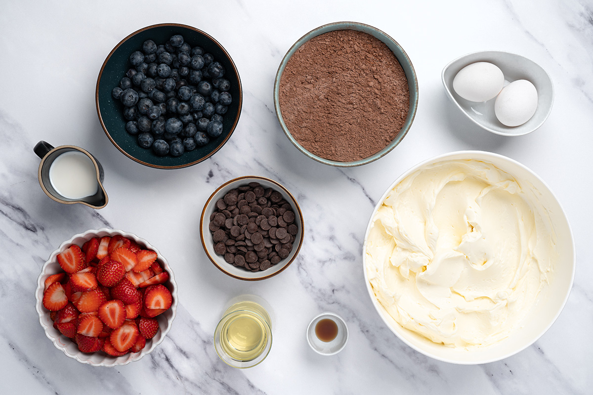 Ingredients for brownie flag recipe including brownie mix, frosting, berries, eggs and chocolate chips.