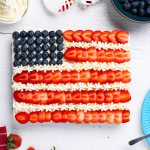 Finished American flag brownies topped with strawberries, blueberries and frosting on a white table.