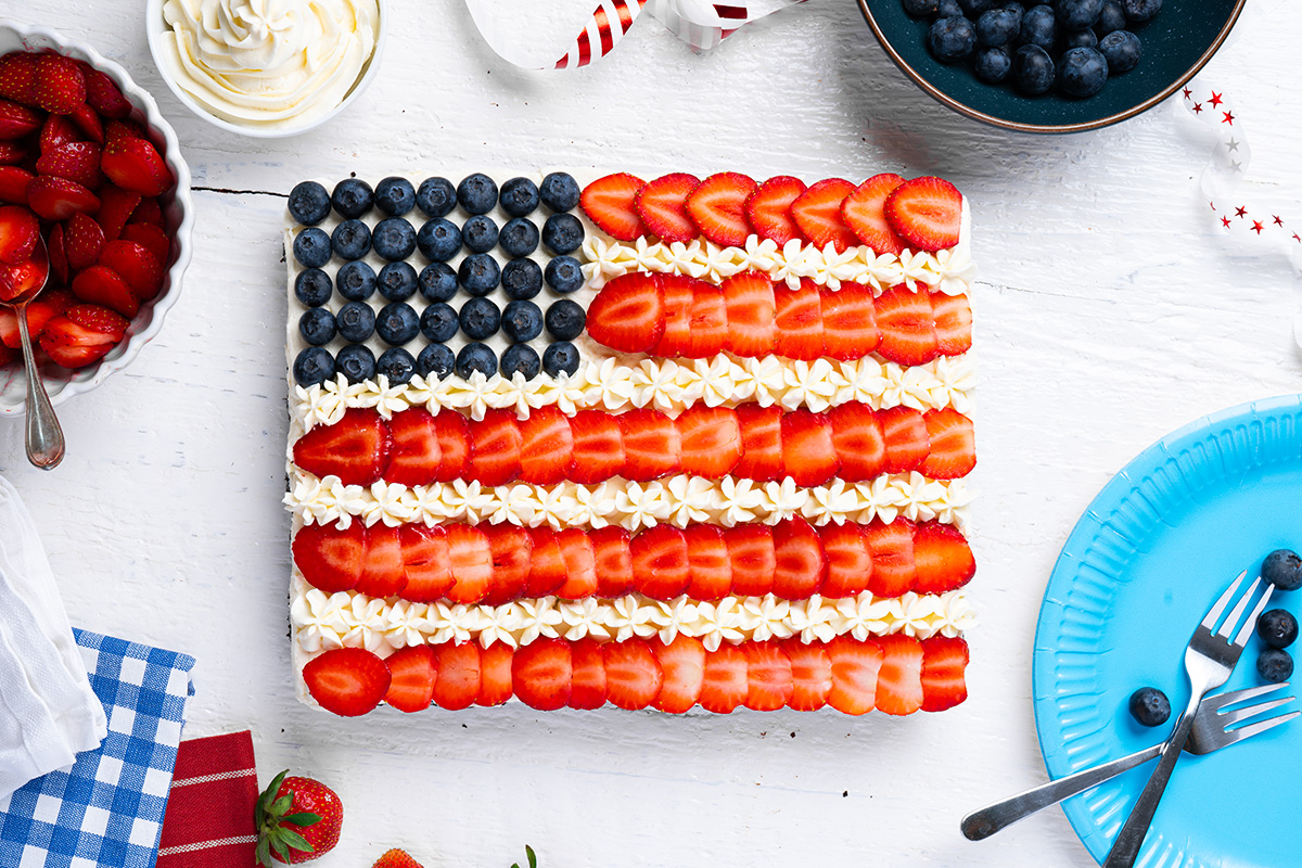 Finished American flag brownies topped with strawberries, blueberries and frosting on a white table.