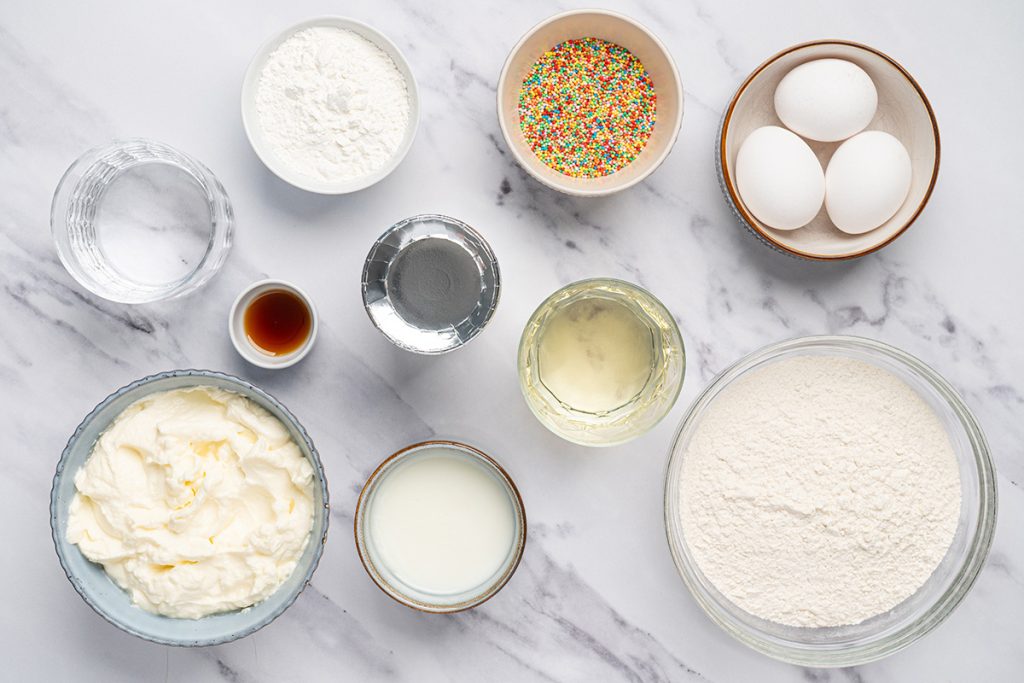 Ingredients for viral dot cakes including cake mix, pudding mix, eggs, frosting and sprinkles.