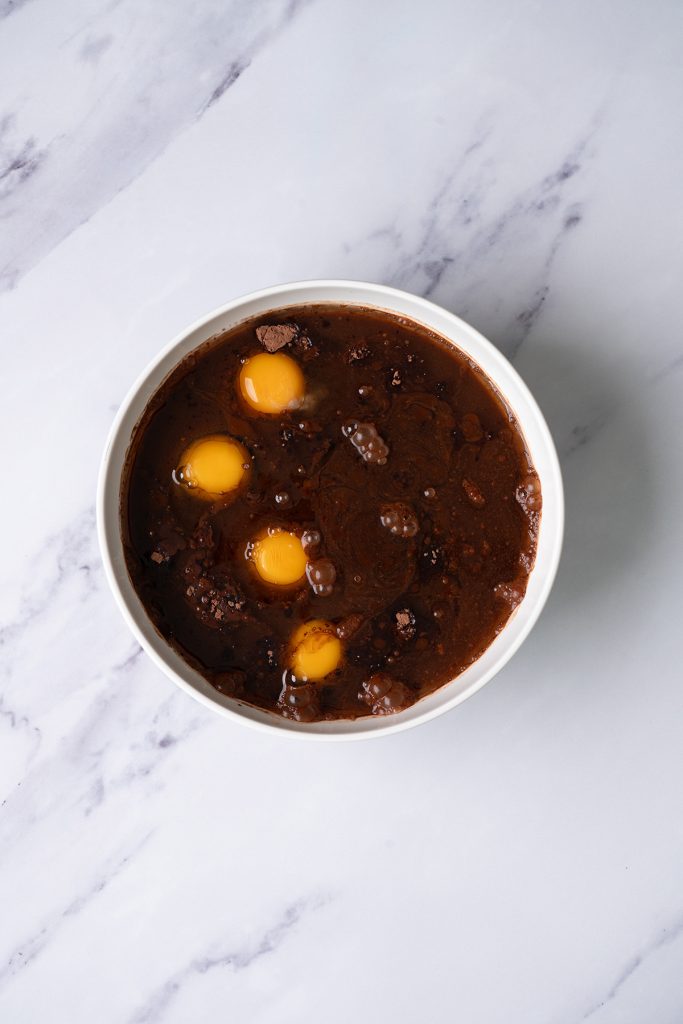 Eggs added to chocolate cake mix and brownie mix batter in a large bowl.
