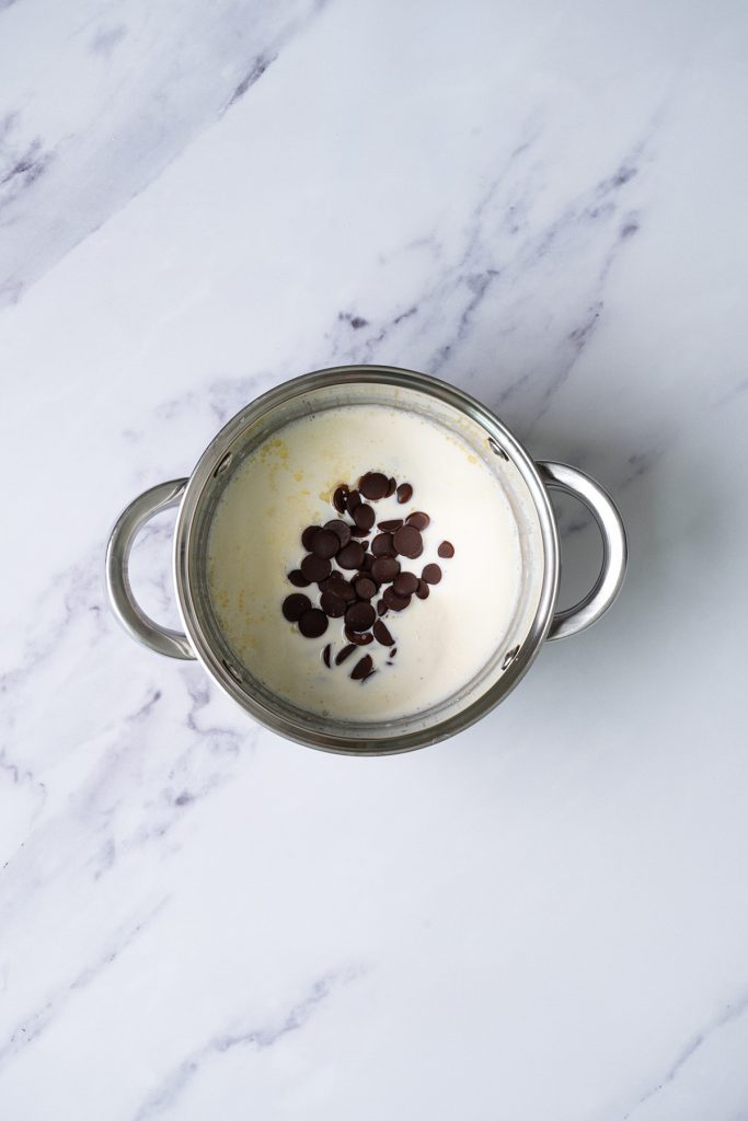 Semi-sweet chocolate chips added to warm cream in a saucepan for homemade chocolate ganache.