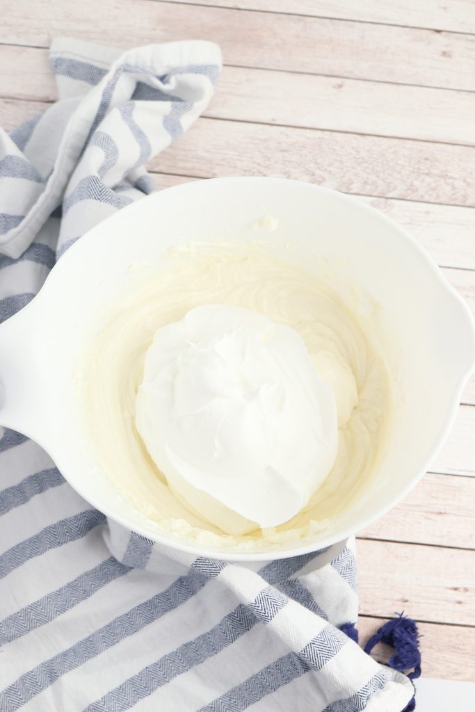 Cheesecake filling with whipped topping added in a white mixing bowl.