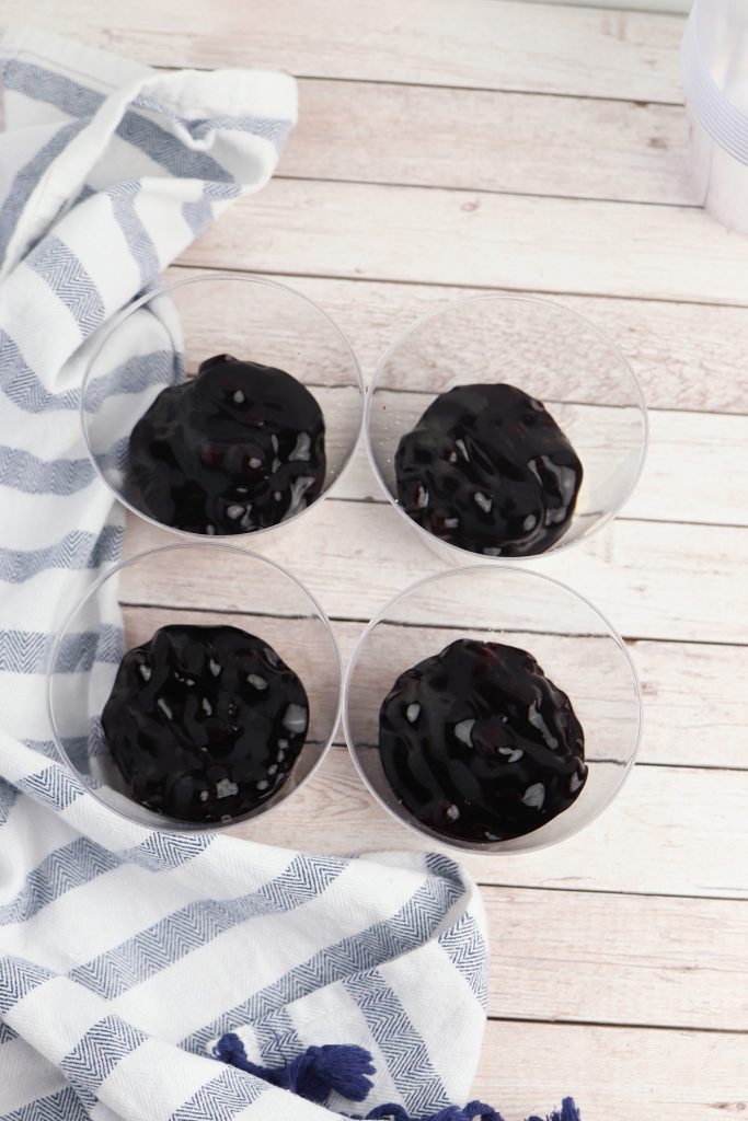 Blueberry pie filling spooned into clear cups for red white and blue cheesecake desserts.