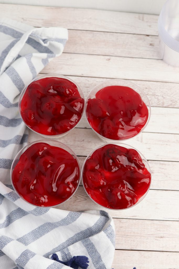 Strawberry pie filling layered in clear dessert cups for patriotic no bake cheesecake cups.
