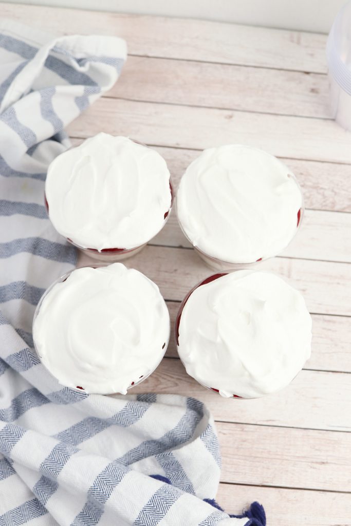 Four no bake cheesecake cups with a smooth layer of whipped topping spread over the top.