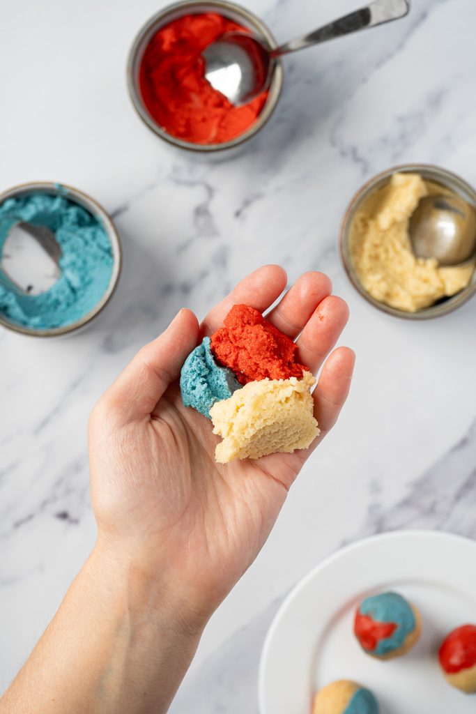 Red, white and blue sugar cookie dough pieces held in a hand before rolling.