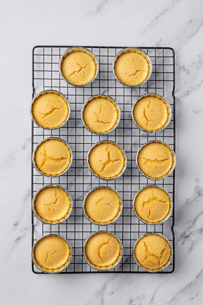 Baked mini vanilla cakes cooling in ramekins on a wire rack.