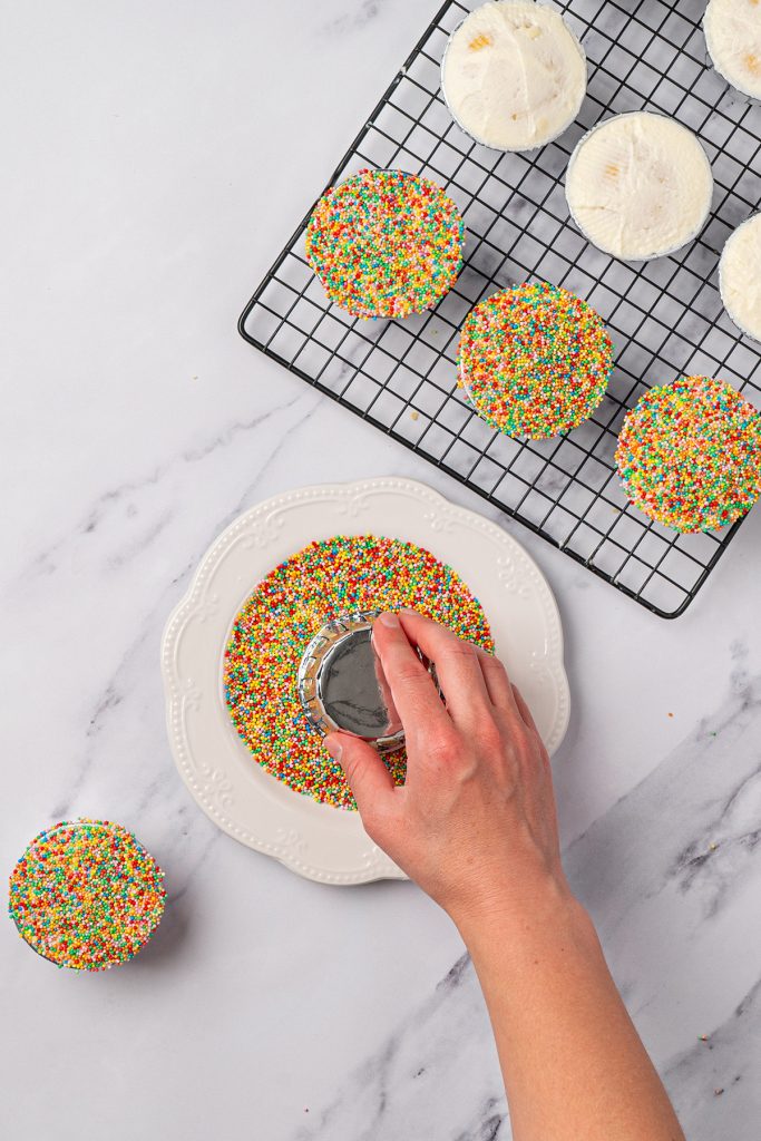 Frosted mini cake pressed into colorful nonpareil sprinkles.