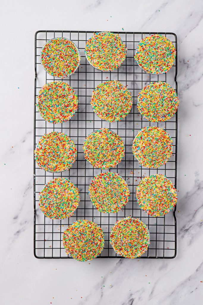 Finished viral dot cakes covered in rainbow sprinkles on a cooling rack.