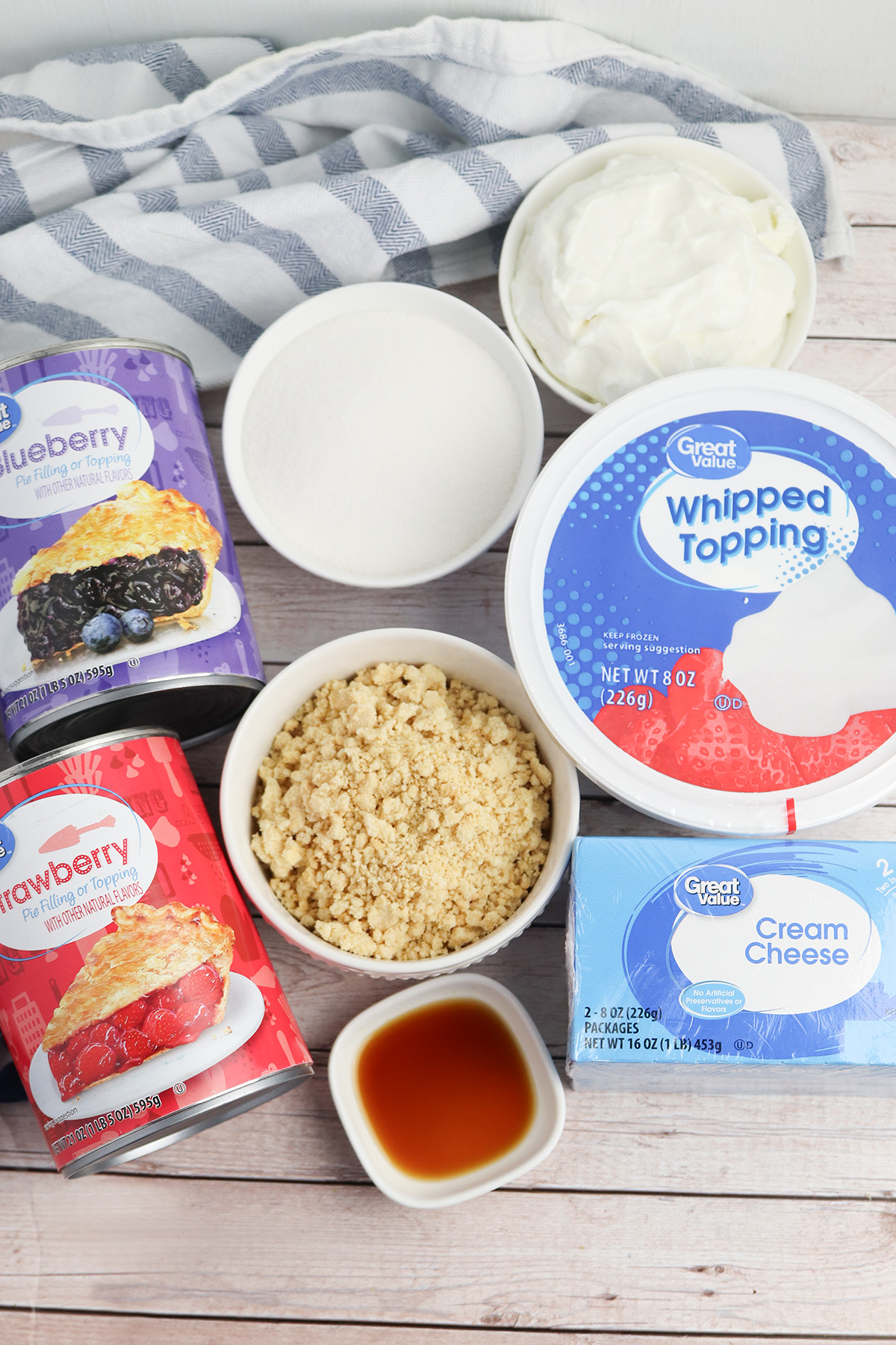 Ingredients for patriotic no bake cheesecake cups including cream cheese, whipped topping, pie fillings, sugar, vanilla, sour cream, and cookie crumbs.