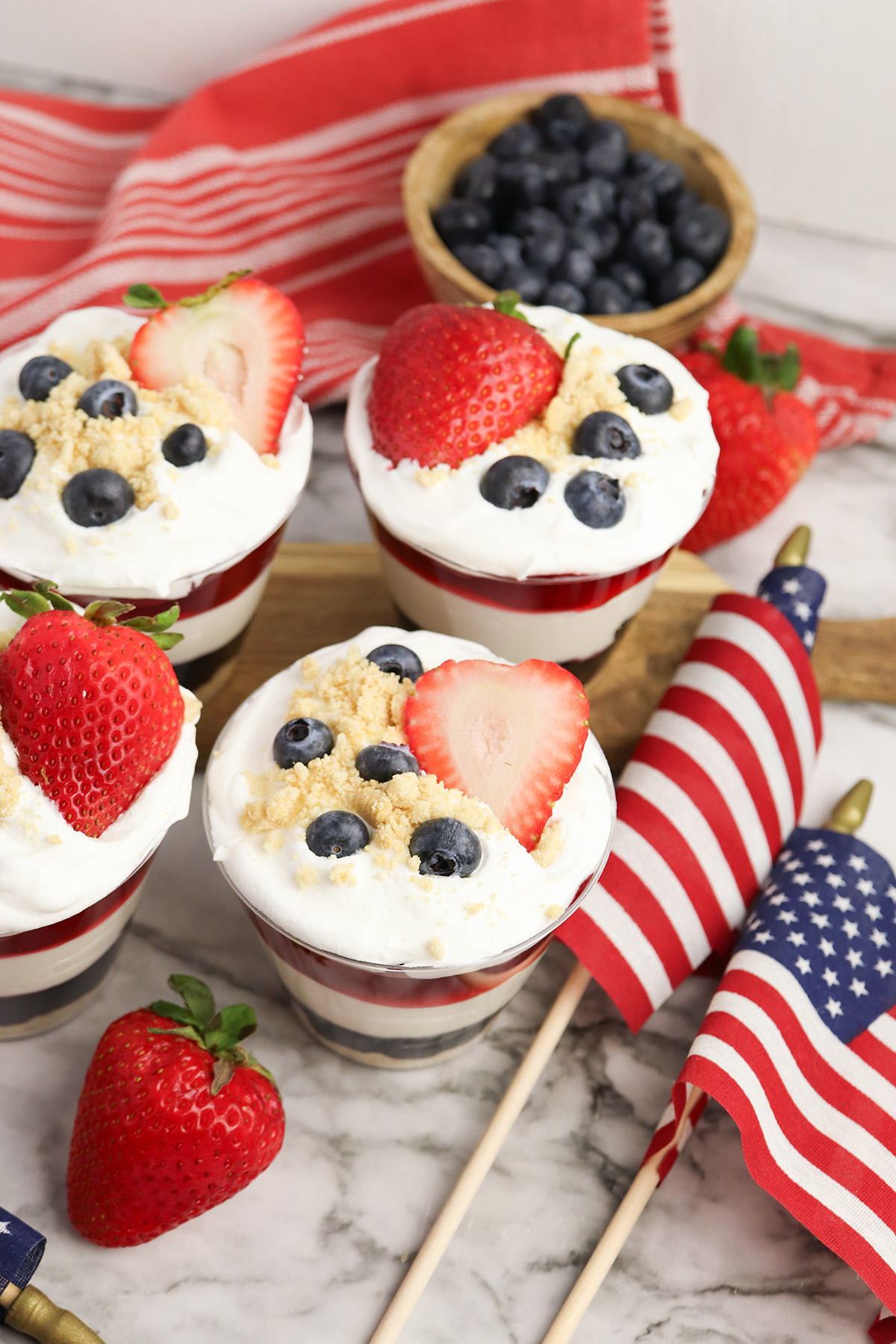 Red white and blue no bake cheesecake cups topped with strawberries, blueberries, and golden Oreo crumbs.
