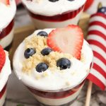 Close up of a 4th of July no bake cheesecake cup with blueberry, cheesecake, strawberry, and whipped topping layers.