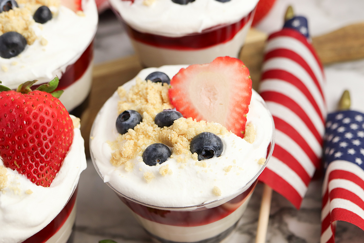 Close up of a 4th of July no bake cheesecake cup with blueberry, cheesecake, strawberry, and whipped topping layers.
