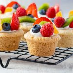 Fruit pizza sugar cookie cups topped with cream cheese frosting and fresh berries.