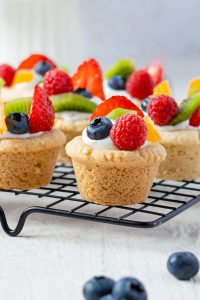 Fruit pizza sugar cookie cups topped with cream cheese frosting and fresh berries.