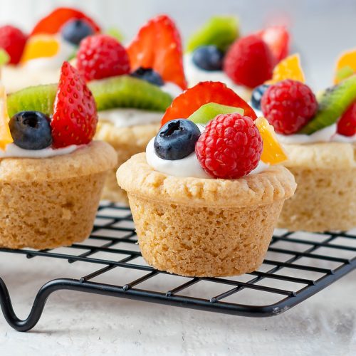 Fruit pizza sugar cookie cups topped with cream cheese frosting and fresh berries.