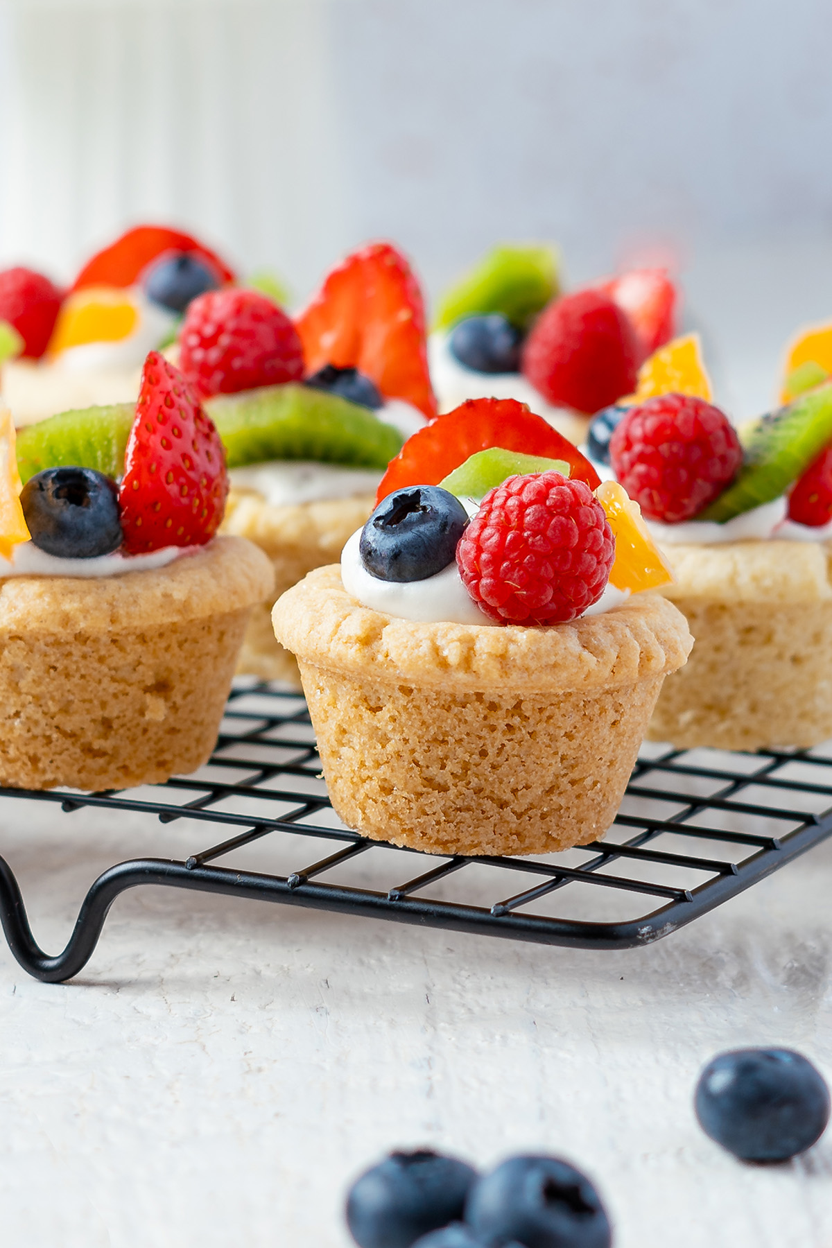 Fruit pizza sugar cookie cups topped with cream cheese frosting and fresh berries.