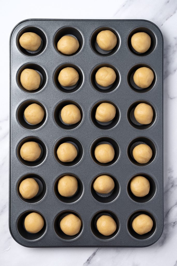 Sugar cookie balls in a mini muffin pan for easy fruit pizza cookie cups.